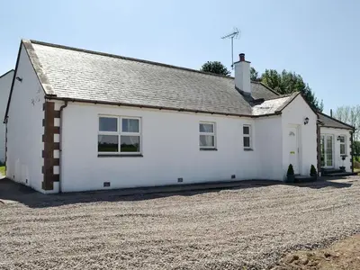 a white cottage on a gravel driveway at Curlew Cottage in Dinwoodie Mains