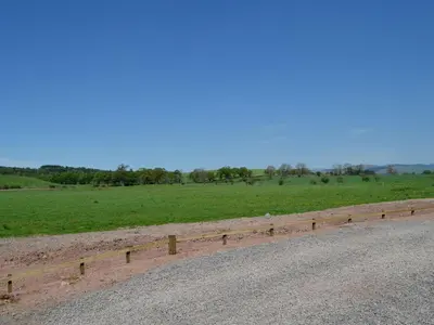 a fence on the side of a road next to a field at Curlew Cottage in Dinwoodie Mains