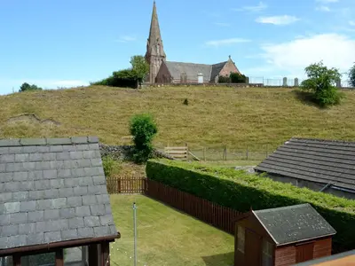 a church on top of a grassy hill with houses at Westlin in Penpont