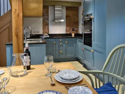 a blue kitchen with a wooden table with plates and glasses at The Barn in Greystoke