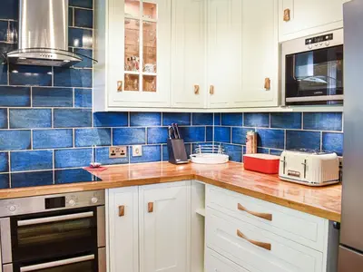 a kitchen with white cabinets and blue tiles at Jane Eyre Cottage in Keswick