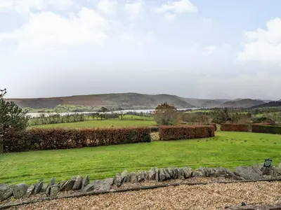 a grassy field with a stone wall and mountains in the background at Mell Fell in Watermillock
