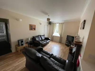 a living room with a leather couch and a television at Belton House Holiday Home in Wanlockhead