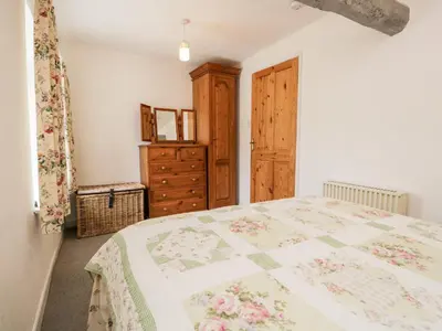 a bedroom with a large bed and a wooden cabinet at Beckfold Cottage in Broughton in Furness