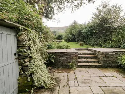 a garden with a stone wall and a white door at Beckfold Cottage in Broughton in Furness