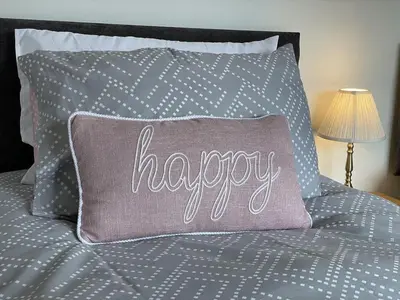 a pillow with the word happy sitting on a bed at Fairbank in Keswick
