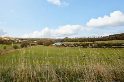 a fence in a field with a river in the background at Camerton Hall Cottage in Workington