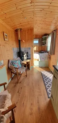 a living room with a wooden ceiling with a stove at Fauld O Wheat Shepherds Hut , Loch Ken ,Off Grid in Castle Douglas