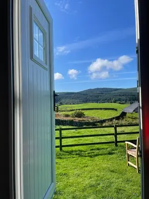 a door open to a view of a field at Fauld O Wheat Shepherds Hut , Loch Ken ,Off Grid in Castle Douglas