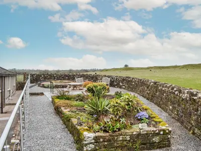a garden with a stone wall and a table and flowers at Scalelands Cottage in Frizington