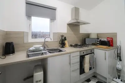 a kitchen with white cabinets and a sink and a window at Troon Golf Apartment in Troon