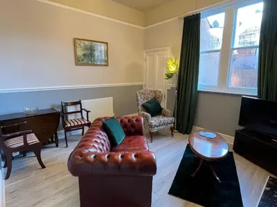 a living room with a leather couch and a piano at Red Gables - Ground Floor in Carlisle