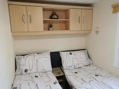 two beds in a small room with wooden cabinets at Holiday Caravan - Sleeps 4 with Parking in Whithorn