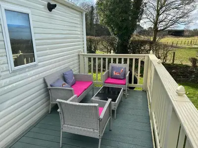 a deck with chairs and tables on a house at 24 The Beeches Caravan Park in Gilcrux