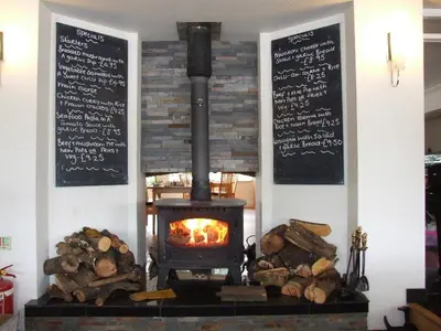 a wood stove with a fire in a room with logs at The Inn on the Loch in Castle Douglas