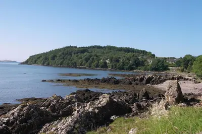 a beach with rocks and the water and trees at The Fish House in Kirkcudbright