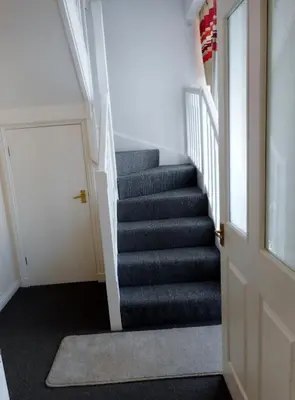 a hallway with a staircase with grey carpet and a door at THE COACH HOUSE in Moffat