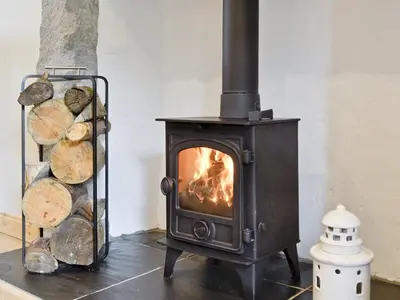 a wood stove in a room with a pile of logs at River Cottage in Bladnoch