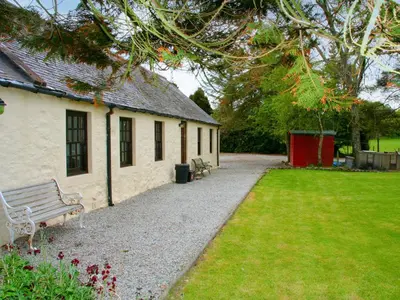 a building with a bench next to a grass yard at The Smithy - Uk38001 in Kirkcowan