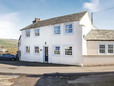 a white house with a car parked in front of it at Old Saddlers Cottage in Ireby