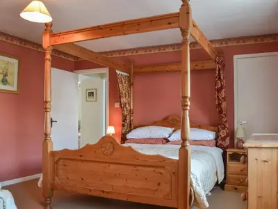 a four poster bed in a bedroom with red walls at Old Saddlers Cottage in Ireby