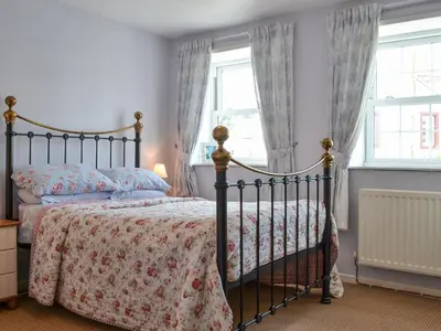 a bedroom with a bed and two windows at Old Saddlers Cottage in Ireby