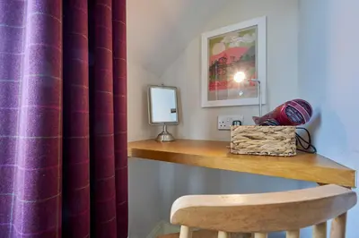a table with a chair and a mirror and a curtain at Howe Keld 6 Second Floor in Keswick