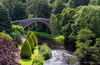 a bridge over a river in a garden with bushes at Beautiful 2 to 3 bed apartment with stunning views! in Ayr