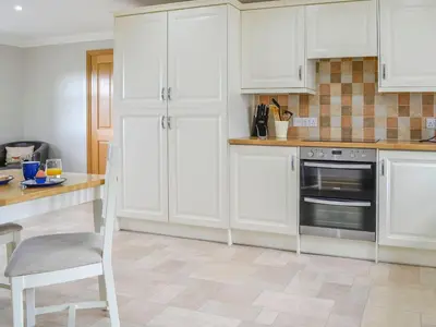 a kitchen with white cabinets and a table with a chair at Knockinaam House in Colfin