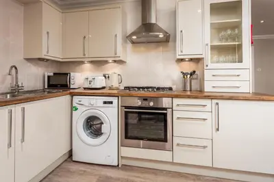 a kitchen with white cabinets and a washing machine at London Gate No1 - Donnini Apartments in Kilmarnock