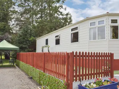 a white house with a fence and flowers in a yard at Tranquillity Lodge in Annbank