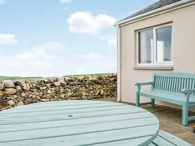 a patio with a table and a bench and a stone wall at Auld Dairy Cottage in Drummore