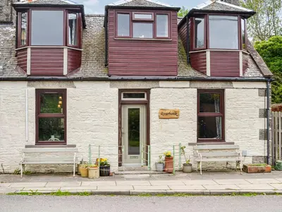 a building with two benches in front of it at Rosebank Cottage in Borgue
