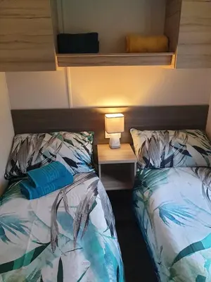 a bedroom with two beds and a table with a lamp at Coral Cabin in Kippford