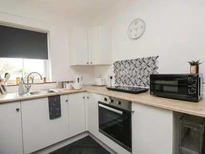 a kitchen with white cabinets and a black microwave at Shoreside Cottage in Wigton