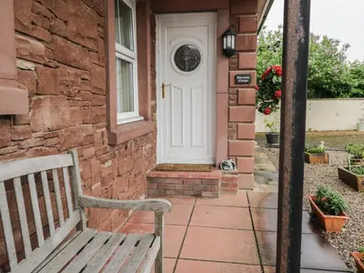 a wooden bench sitting outside of a brick house with a white door at Shoreside Cottage in Wigton