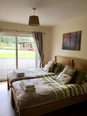 two beds in a room with a large window at Gamepark Wood Holiday Cottage in Castle Douglas