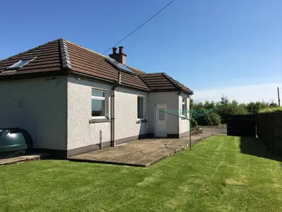 a house with a grass yard in front of it at Gamepark Wood Holiday Cottage in Castle Douglas
