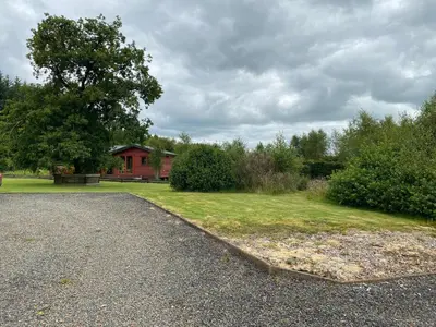 a driveway in front of a house with a tree at Gamepark Wood Holiday Cottage in Castle Douglas
