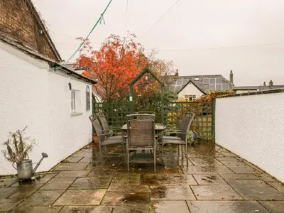 a patio with a table and chairs in the rain at Raphael's Cottage in Keswick