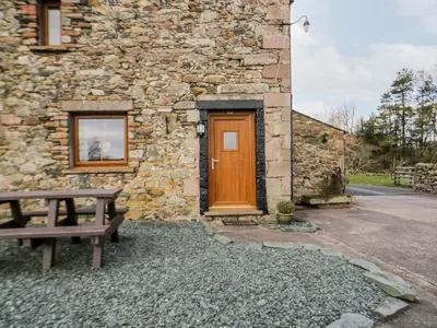 a stone building with a wooden door and a bench at Lavender Cottage in Penrith
