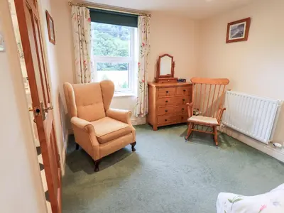 a bedroom with a chair and a dresser and a window at 7 Stybarrow Terrace in Penrith