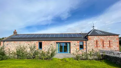 a brick house with solar panels on the roof at The Stables - Luxury Cottage in Dumfries