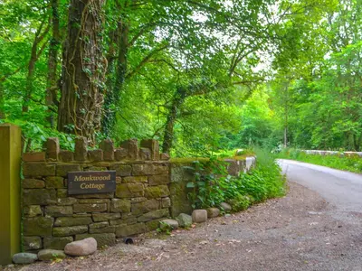 a stone wall with a sign on a road at Monkwood Cottage in Hale