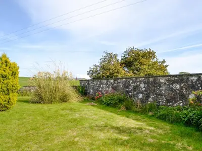 a garden with a stone wall and plants at Culbae Cottage in Whauphill