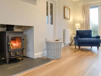 a living room with a fireplace and a blue chair at Culbae Cottage in Whauphill