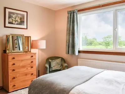 a bedroom with a bed and a window and a chair at High Threave Cottage in Newton Stewart