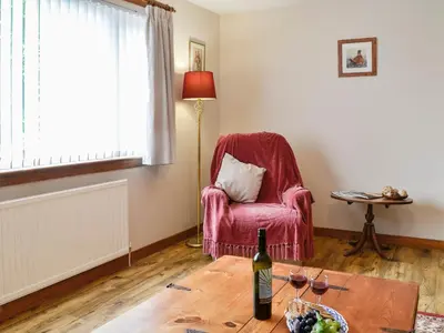 a living room with a chair and a bottle of wine at High Threave Cottage in Newton Stewart