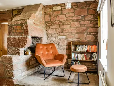 a chair and stool in front of a stone fireplace at Low Moat in Canonbie