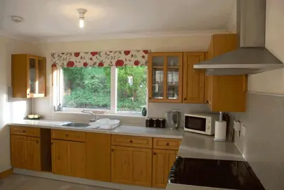 a kitchen with wooden cabinets and a window with a microwave at 3 Bed Bungalow - Sleeps 6 - Pet Friendly - Parking in Drummore